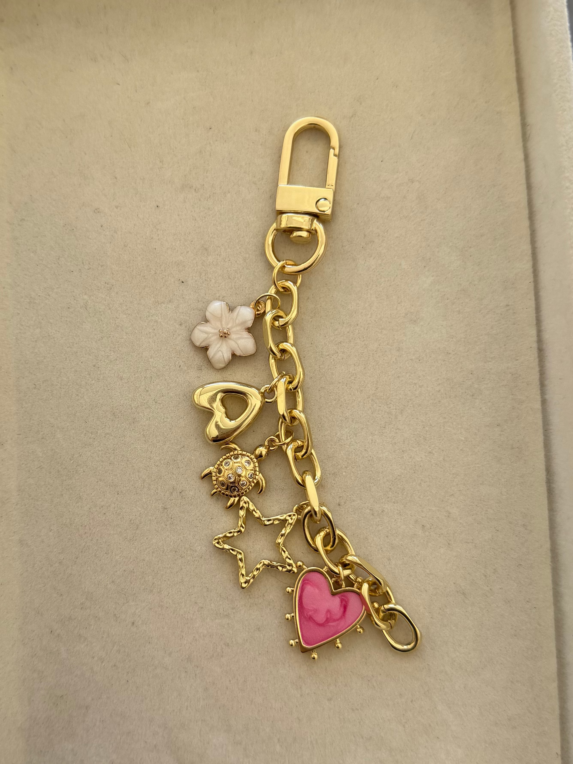 gold bag chain with five charms, pink heart, gold star, turtle, initial A and flower.