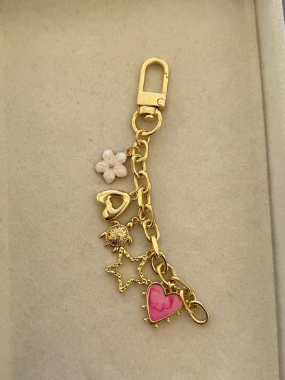 gold bag chain with five charms, pink heart, gold star, turtle, initial A and flower.